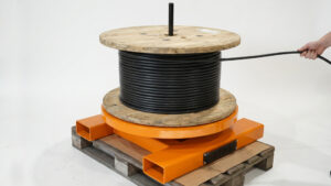 JKS VT 9 Pystypukki – oranssi laakeroitu kelanalusta, jonka päällä on kyljelleen asetettu kaapelikela kaapelin helppoa purkua varten.